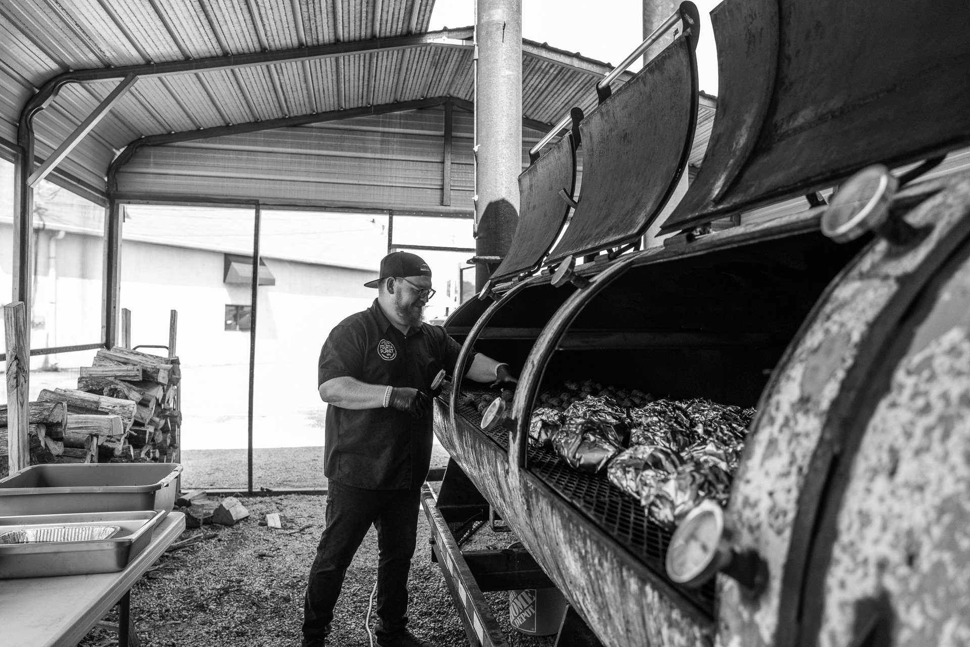 The pitmaster working a row of offset smokers under the carport